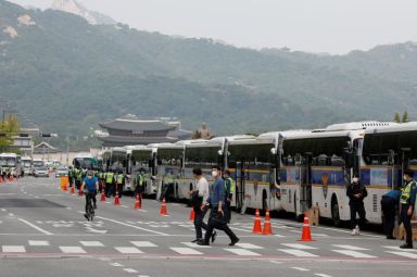 Pedestrians walk past police buses that are parked surrounding the