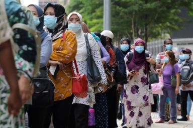 Passengers wearing protective masks wait in line to board a